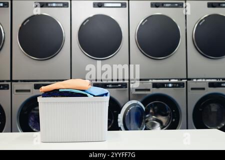 Plan de fond du panier plein de vêtements colorés sur la table pliante dans la buanderie libre-service avec sèche-linge professionnel et machines à laver, espace copie Banque D'Images