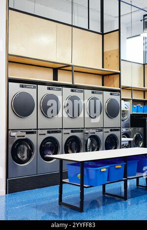 Intérieur de laverie moderne en libre-service avec double rangée de machines à laver professionnelles et de sèche-linge imbriqués sur une table pliante, espace photocopie Banque D'Images