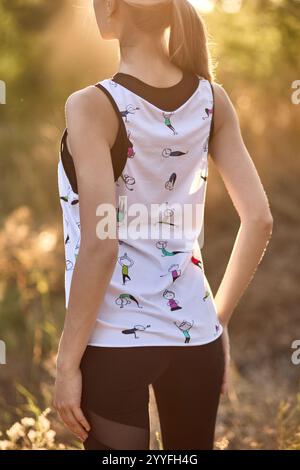 Une femme dans un débardeur de sport avec des imprimés, éclairé par la lumière du soleil tout en se tenant à l'extérieur, représentant un style de vie actif, concept de fitness en plein air Banque D'Images