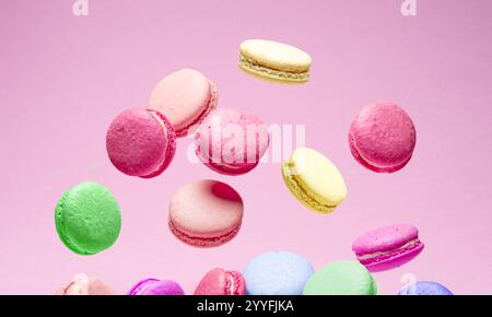 Macarons français colorés tombant isolé sur fond rose. Banque D'Images