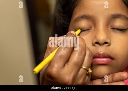 Une jeune fille se fait appliquer son eye-liner, un moment tendre de préparation de beauté. Banque D'Images