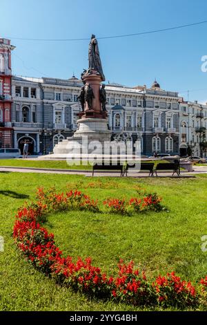 Une statue d'un homme se dresse devant un bâtiment avec une grande disposition de fleurs rouges dans l'herbe Banque D'Images