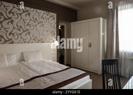 Une chambre avec un lit blanc et une couette marron. Le lit est défait et la chambre est vide Banque D'Images