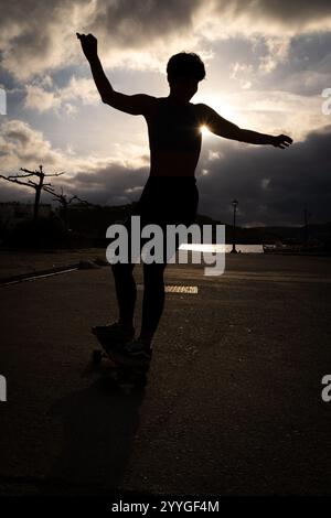 Silhouette d'une jeune fille grecque pratiquer le skateboard dans le port de la ville de Naoussa sur l'île de Paros dans l'archipel des Cyclades en Grèce sur 1 Banque D'Images