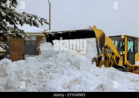 Le chargeur de neige nettoie activement les gros tas de neige des rues résidentielles pendant la tempête hivernale. Banque D'Images
