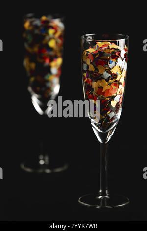 Deux verres à champagne remplis de confettis colorés sur fond noir Banque D'Images