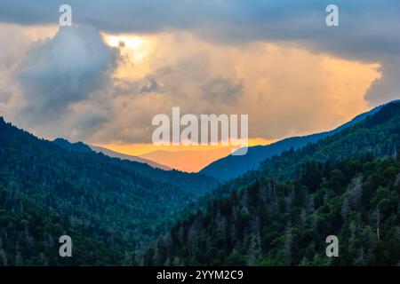 Le ciel est rempli de nuages et le soleil se couche. Les montagnes en arrière-plan sont couvertes d'arbres Banque D'Images