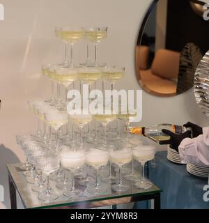 Imposante pyramide de verres à champagne remplis de bulles, élégamment disposés sur un fond rose éclairé, parfait pour les célébrations haut de gamme, les mariages Banque D'Images
