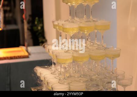 Imposante pyramide de verres à champagne remplis de bulles, élégamment disposés sur un fond rose éclairé, parfait pour les célébrations haut de gamme, les mariages Banque D'Images