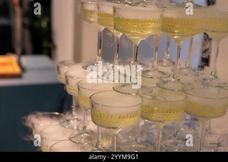 Imposante pyramide de verres à champagne remplis de bulles, élégamment disposés sur un fond rose éclairé, parfait pour les célébrations haut de gamme, les mariages Banque D'Images