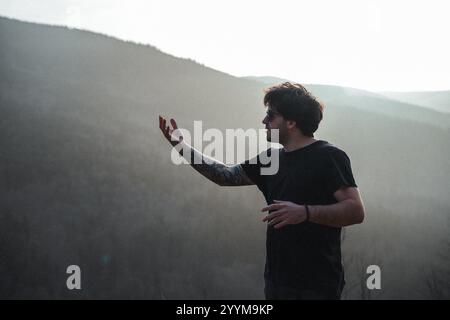 Dans une photo captivante en noir et blanc, un homme vêtu d'une chemise noire se tient confiant devant une montagne majestueuse en toile de fond Banque D'Images