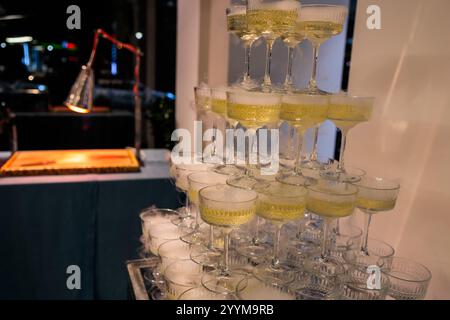 Imposante pyramide de verres à champagne remplis de bulles, élégamment disposés sur un fond rose éclairé, parfait pour les célébrations haut de gamme, les mariages Banque D'Images