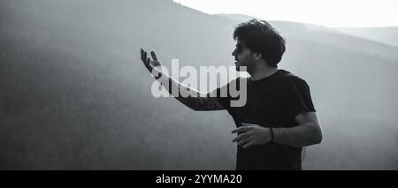 Dans une photo captivante en noir et blanc, un homme vêtu d'une chemise noire se tient confiant devant une montagne majestueuse en toile de fond Banque D'Images