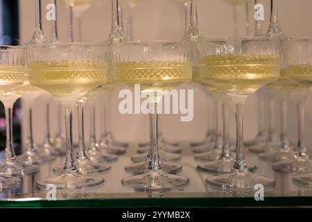 Imposante pyramide de verres à champagne remplis de bulles, élégamment disposés sur un fond rose éclairé, parfait pour les célébrations haut de gamme, les mariages Banque D'Images