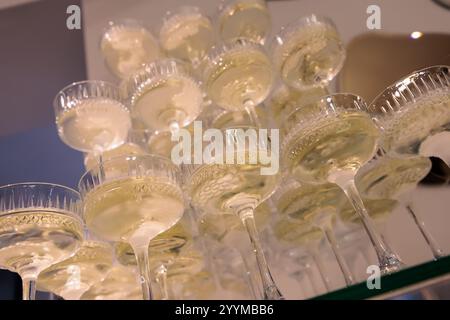 Imposante pyramide de verres à champagne remplis de bulles, élégamment disposés sur un fond rose éclairé, parfait pour les célébrations haut de gamme, les mariages Banque D'Images