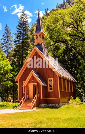 Une petite église rouge avec un clocher se trouve dans un champ herbeux. L'église est entourée d'arbres et il est dans un cadre paisible et serein Banque D'Images