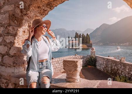 Jeune femme profitant de la vue pittoresque de notre dame de l'île des rochers depuis une fenêtre en pierre à Perast, Monténégro Banque D'Images