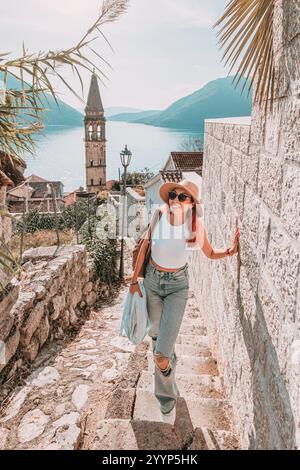 Jeune femme touriste explorant les charmantes rues de Perast, une ville côtière historique du Monténégro, avec son église emblématique et une vue imprenable sur la baie Banque D'Images