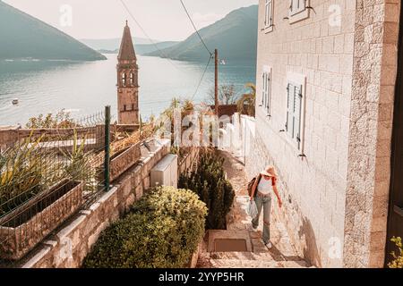 Jeune femme touriste explorant les charmantes rues de Perast, une ville côtière historique du Monténégro, avec son église emblématique et une vue imprenable sur la baie Banque D'Images