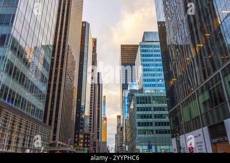 Gratte-ciel s'élevant le long de la rue animée de New York, reflétant la lumière dorée du coucher du soleil sur le ciel nuageux. New York. ÉTATS-UNIS. Banque D'Images