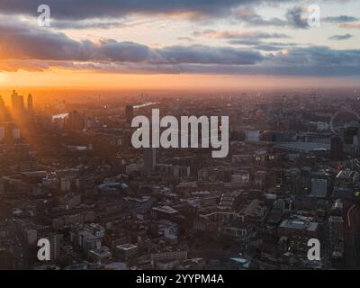 L'image montre une vue aérienne de Londres au coucher du soleil, avec le London Eye et la Tamise. La lueur chaude met en valeur le paysage urbain et cl Banque D'Images