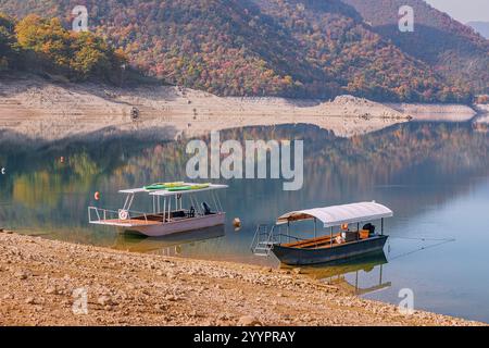 29 octobre 2024, Pluzine, Monténégro : deux bateaux de plaisance sont amarrés près de la rive d'un lac tranquille, avec les couleurs vibrantes du feuillage d'automne m Banque D'Images
