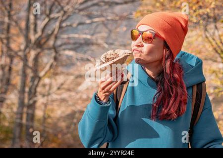 Jeune femme randonneuse sentant un gros champignon lors d'un voyage de recherche de nourriture dans une forêt d'automne Banque D'Images