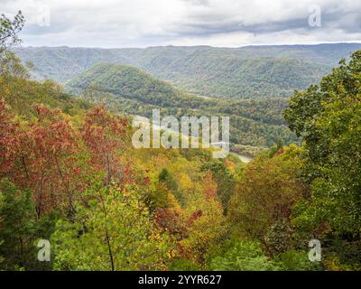 Les montagnes couvertes d'arbres du parc national de New River gorge, en Virginie-occidentale, affichent des couleurs d'automne sous un ciel nuageux, avec des ponts distants ajoutant de Banque D'Images