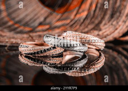 couleur tendance 2025. Les anneaux de mariage sont reflétés dans le miroir. Un ensemble de trois anneaux sur un fond de plumes de paon. Bagues en or et en argent avec Banque D'Images