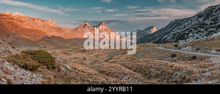 Vue panoramique sur une route sinueuse au coucher du soleil coupant à travers le paysage pittoresque du parc national de Durmitor, Monténégro, avec ses sommets majestueux luisants Banque D'Images