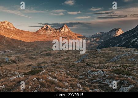 Vue panoramique sur une route sinueuse au coucher du soleil coupant à travers le paysage pittoresque du parc national de Durmitor, Monténégro, avec ses sommets majestueux luisants Banque D'Images