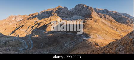 Route sinueuse serpentant à travers une vallée dans les montagnes de Durmitor, Monténégro, menant vers des sommets imposants baignés de soleil doré Banque D'Images