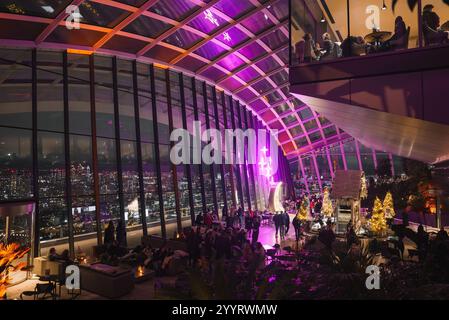 Le Sky Garden de Londres présente des décorations de Noël, des arbres illuminés et une cabane confortable. De grandes fenêtres révèlent l'horizon de la ville la nuit. Banque D'Images