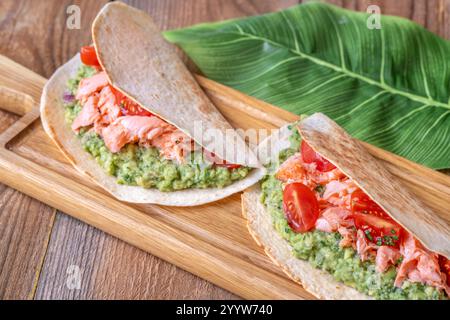 Deux tacos remplis de guacamole, de saumon cuit au four et de tomates sur une table rustique en bois Banque D'Images