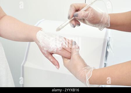 Main féminine recevant un traitement cosmétique avec de la crème appliquée par un professionnel ganté. Banque D'Images