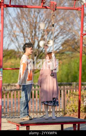Un couple dans la vingtaine s'amuse à jouer avec l'équipement de terrain de jeu dans un grand parc de la ville de Handa, préfecture d'Aichi en automne. Banque D'Images