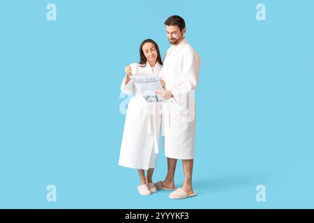 Couple aimant dans des peignoirs avec journal de lecture de café sur fond bleu Banque D'Images