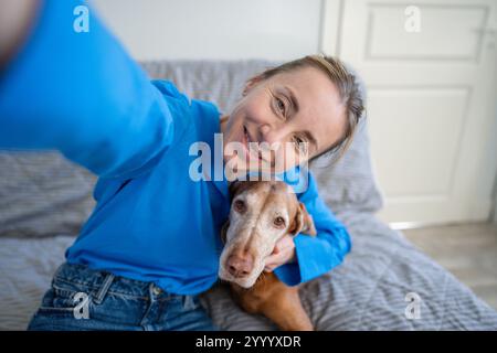 Selfie de femme souriante embrassant le chien Vizsla sur le canapé à la maison. Affection du propriétaire, soins pour animaux de compagnie, amour Banque D'Images