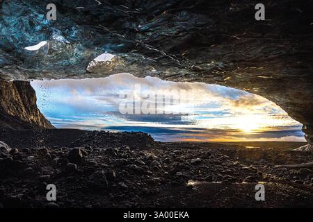 Une vue impressionnante depuis l'intérieur d'une grotte de glace montre des teintes vives du ciel et un terrain accidenté au coucher du soleil. La lumière du soleil projette de belles ombres à travers le lan Banque D'Images