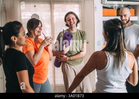 Groupe diversifié de sportifs parlant, riant. Se reposer et boire compagnon après le cours de yoga dans une atmosphère sociale conviviale au club de yoga. Banque D'Images