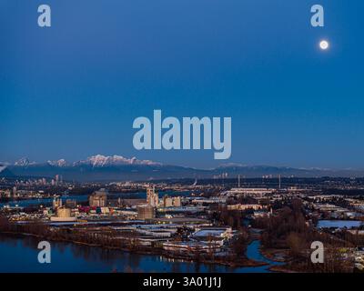 Delta BC Canada - 11 février 2025 : coucher de soleil au bord de l'eau du parc régional de l'île Deas avec lever de la lune sur la montagne Banque D'Images