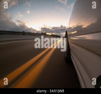 Une voiture roule sur une route avec un coucher de soleil en arrière-plan Banque D'Images