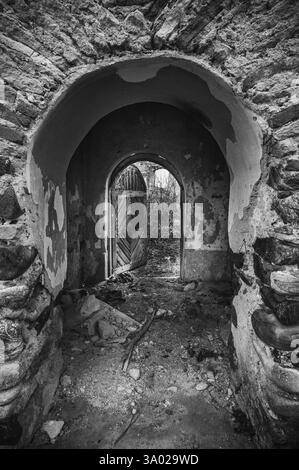 À travers un portail voûté, un aperçu de la décomposition : un passage oublié avec des pierres altérées et une porte ouverte, invitant à l'exploration d'une époque révolue. Banque D'Images