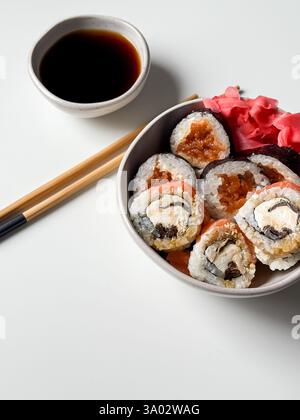Rouleaux de sushi dans un bol avec du gingembre rose et de la sauce soja et des bâtonnets en bois sur la table blanche Banque D'Images