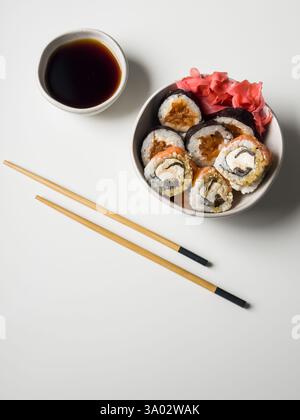Rouleaux de sushi dans un bol avec du gingembre rose et de la sauce soja et des bâtonnets en bois sur la table blanche Banque D'Images