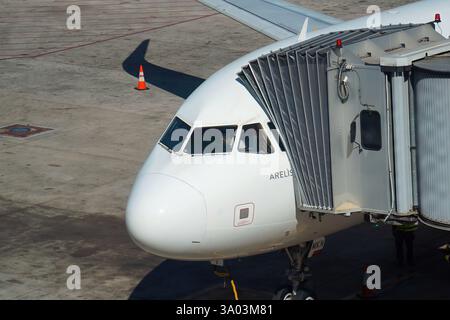 Gros plan avant vol du cockpit et des fenêtres du jet blanc avec pilote à l'intérieur, stationné sur l'aire de trafic de l'aéroport amarré à la passerelle piétonne vue depuis le terminal. Banque D'Images
