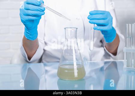 Tests en laboratoire. Un scientifique égoutte l'échantillon de la pipette dans le flacon à table à l'intérieur, gros plan Banque D'Images