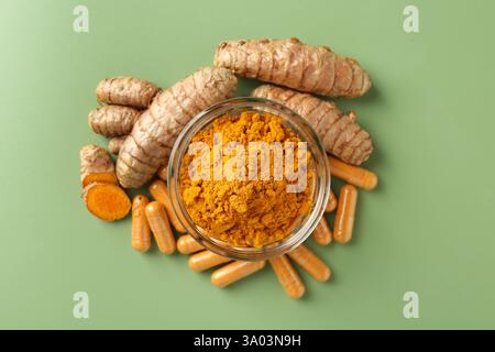 Poudre de curcuma dans un bol, racines et capsules sur fond vert, plat Banque D'Images