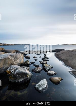 Les eaux calmes reflètent le ciel le long de la côte accidentée à l'extérieur de Gothenburg, où les rochers éparpillés créent un environnement tranquille pour les amoureux de la nature. Banque D'Images