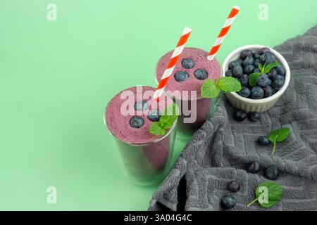 Deux smoothies aux myrtilles et un bol blanc de myrtilles. Les smoothies sont dans de grands verres avec des pailles rouges et blanches surmontées de bleuets et Banque D'Images